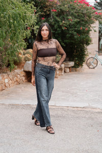 Ce haut à manches longues est confectionné dans une dentelle brune fine et transparente au motif floral délicat, doté d'une encolure haute et d'un ourlet droit ajusté à la taille. Il est superposé à un top bandeau opaque marron chocolat qui couvre la poitrine, créant un effet de transparence sur les manches et le décolleté. Le pantalon est un jean bicolore avec un délavage bleu moyen sur le devant et des panneaux bleu foncé sur les côtés, avec une braguette à bouton-pression et des passants de ceinture.